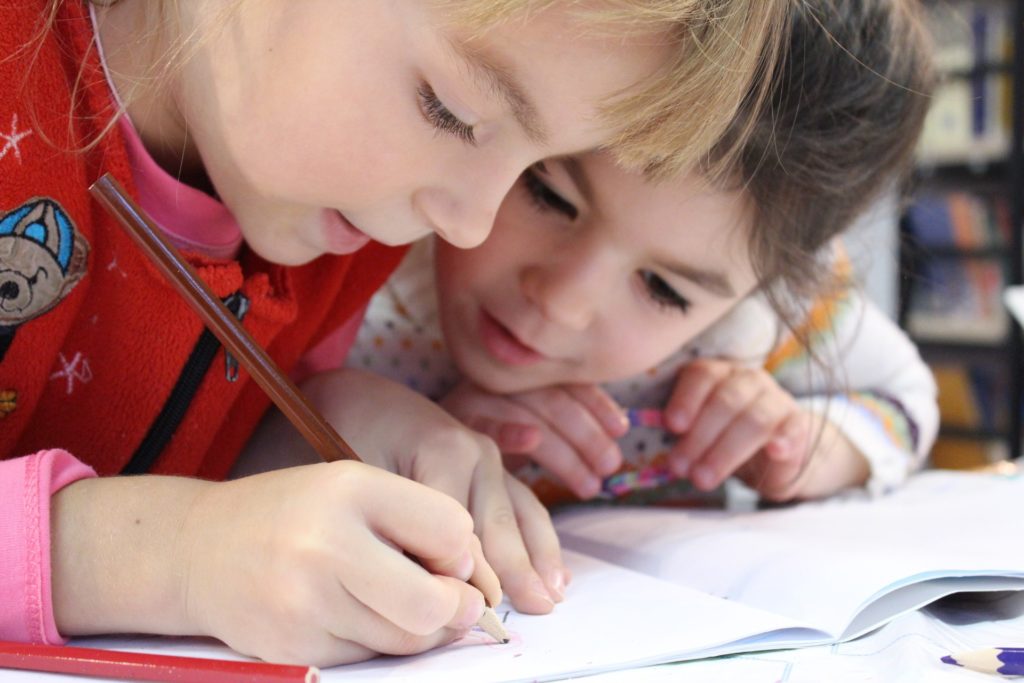 two young girls at a desk looking at and writing in a notebook