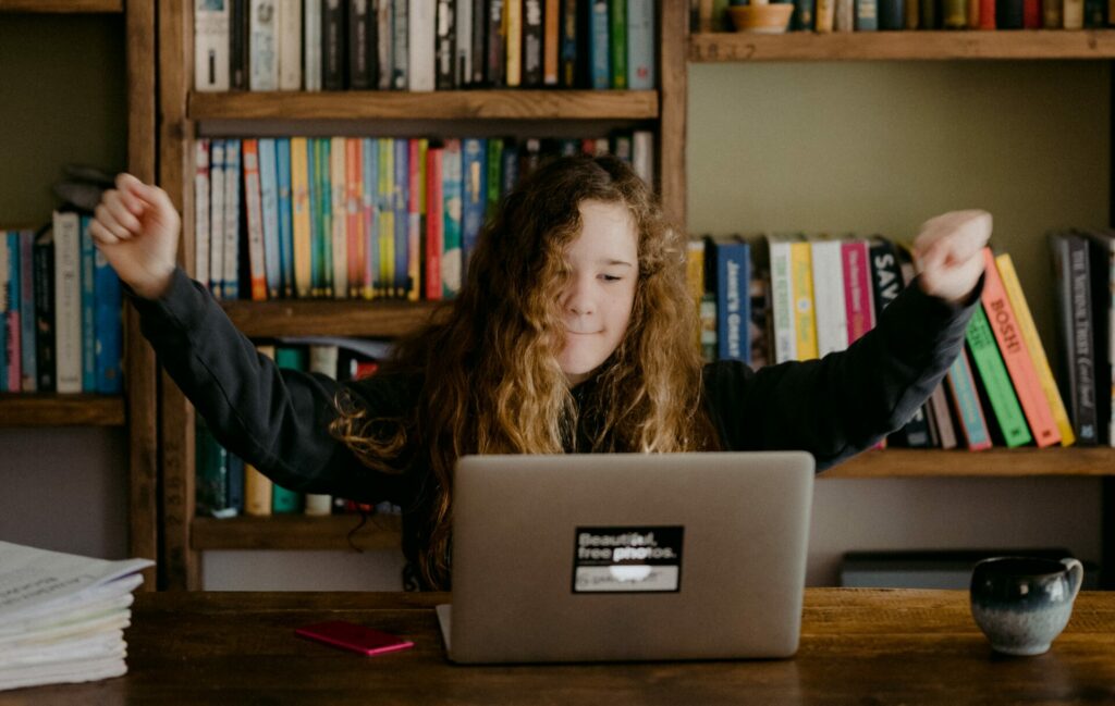 Decorative: young person looking at laptop holding arms aloft in celebration