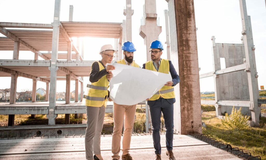Image of three people dressed in hi-viz jackets and hard hats on a building site looking at a large map.