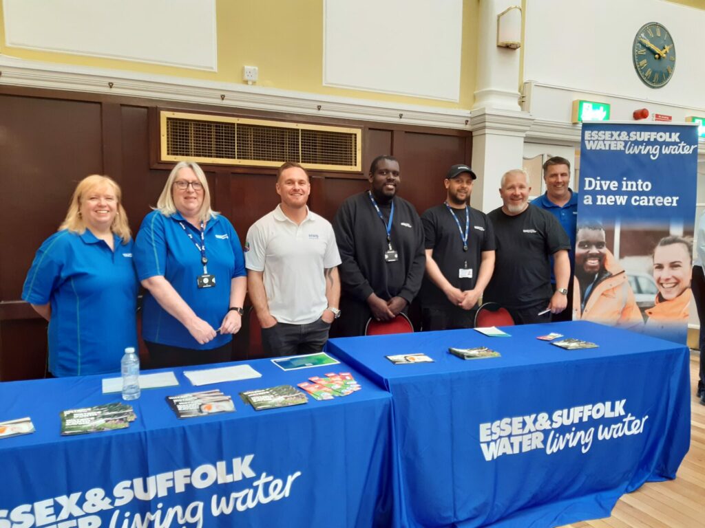 Seven members of the Essex and Suffolk Water team stand smiling behind stand at the fair.