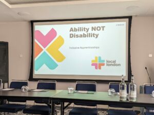 Picture of tables and chairs for the panel with big screen behind introducing the Ability not Disability workshop