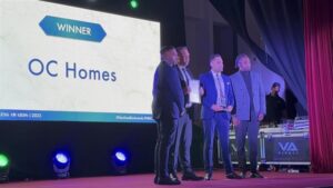 Award winners OC Homes hold their prize on stage in front of an audience.