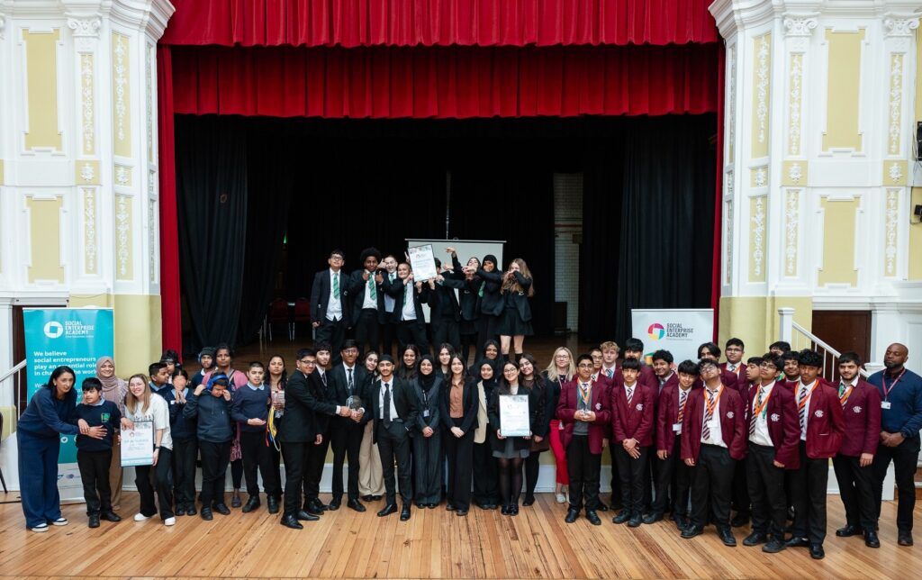 Group shot of students who took part with teachers in front of a stage.