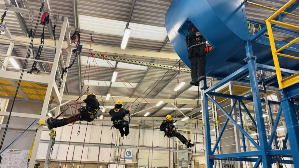 Photo of students at Enfield facility where they are learning how to work safely at heights suspended by harnesses.