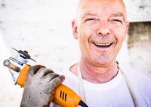 Man smiling holding a hand tool.